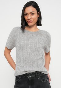 Ανοιχτό γκρι πουλόβερ με κοντά μανίκια, υφή με κοτσίδες και στρογγυλή λαιμόκοψη, σε συνδυασμό με μαύρη τζιν φούστα με ψηλή μέση.