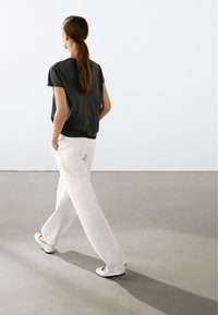 Sort kortærmet top parret med hvide stribede vide bukser. Outfittet har en afslappet pasform, sidelommer og enkle flade sko.