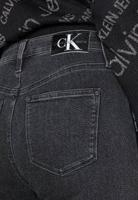 Jeans de mezclilla slim-fit en gris oscuro con una etiqueta negra de Calvin Klein en la cintura trasera y dos bolsillos traseros con detalles de costura sutiles.