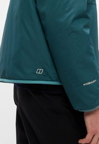 Sinineroheline jopevarrukas ja serv, millel on "HydroLoft" logo, kantud mustade pükste kohal, parempoolne käsi lõdvestunult kõrval valgel taustal.