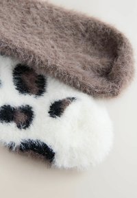 Ruskea pörröinen sukka päällekkäin valkoisen pörröisen sukan kanssa, jossa on mustia ja ruskeita laikkuja. Pehmeä rakenne, pyöreä varvas ja kaksivärinen muotoilu.