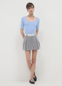 Top aderente azzurro chiaro a maniche corte abbinato a una mini gonna grigia plissettata con tasche laterali e una cintura bianca. Scarpe nere basse completano il look.