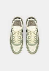 Zapatillas verdes y crema con puntera perforada, forma redondeada, detalles en ante texturizado y logo negro contrastante en los lados.