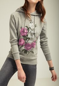 Felpa grigia con stampa floreale in rosa e bianco, con il testo 'Punk Rock Love'. Composizione in misto cotone con vestibilità rilassata e cappuccio con cordino.