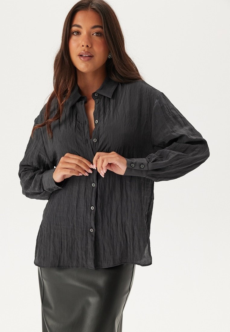 Camicia button-up in tessuto nero crinkled con vestibilità relax, dotata di colletto a punta, maniche lunghe e bottoni discreti lungo il davanti.