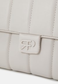 Gros plan sur un sac en cuir blanc matelassé avec des panneaux verticaux cousus et un rabat fermé par un logo RF en relief.