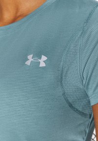 Teal sportströja med ett texturerat mönster och korta ärmar. Har en vit Under Armour-logotyp på bröstet och kontrasterande sömmar.