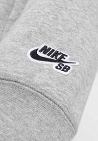 Felpa in cotone grigio chiaro con logo Nike SB ricamato in bianco e nero sulla manica, con una texture morbida e polsini a costine.