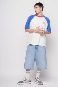 Tričko s krátkým rukávem v bílé a modré barvě s červeným výstřihem, spárované s lehkými džíny šortkami a šedými teniskami s bílými detaily a pruhovanými ponožkami.