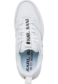 White sneaker with perforated upper, flat laces, and branded tongue. Features light blue insole and black text. Rounded toe and rubber sole.
