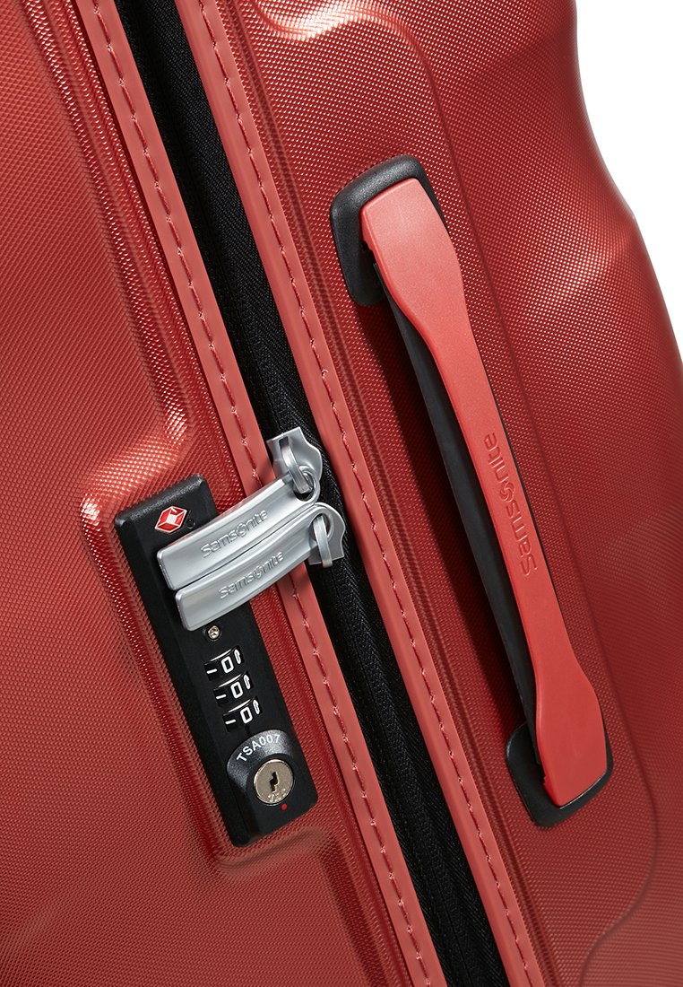 Maleta rígida roja con una superficie texturizada, cremalleras dobles, un candado de combinación y un asa lateral resistente para un transporte fácil.