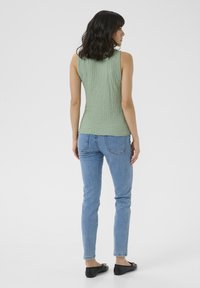 Grøn, struktureret ærmeløs top, tætsiddende design, parret med lyseblå jeans og sorte flade sko. Simpel og moderne stil.