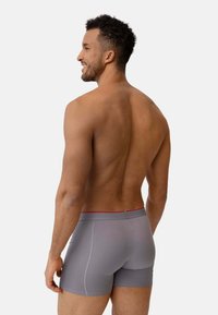 Grå kalsonger med röd midjeband, med en slät textur och åtsittande design, sedd bakifrån mot en ljus bakgrund.