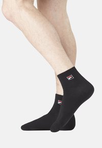 Chaussettes noires de cheville en coton avec une texture douce. Présente un petit logo rouge et blanc sur le côté.