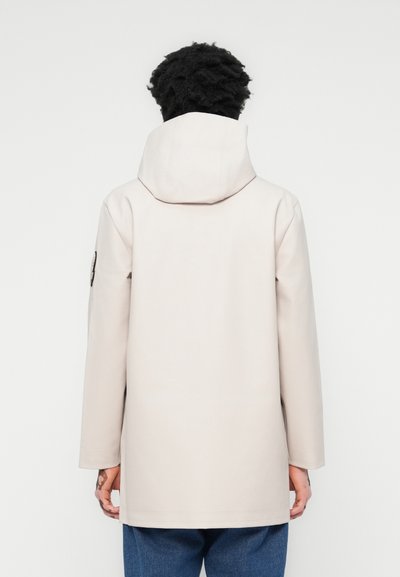 Beige vanntett jakke med hette, som har en rett passform, lange ermer og et minimalistisk design. Inkluderer en liten logo på ermet.