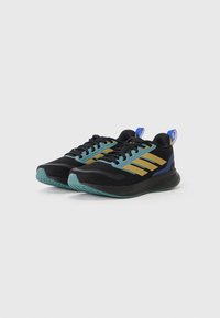 Baskets noires de sport avec des accents en bleu sarcelle, des rayures dorées et une semelle texturée. Présentent un col rembourré et une tirette bleue au talon.