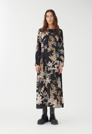 Lungo vestito nero con motivo floreale in colori pastello, caratterizzato da maniche lunghe e una silhouette svasata, abbinato a stivaletti neri alla caviglia.