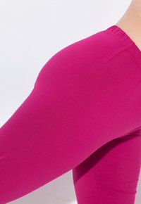 Fuchsia leggings with a smooth, stretchy texture and an elastic waistband, shown from the side to highlight the fit and color.