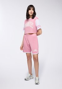 Różowy zestaw składający się z crop topu i szortów z białymi akcentami, z napisem "Los Angeles". Teksturowany materiał, sportowy krój i luźny fason.