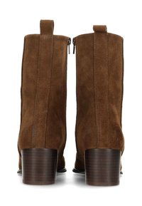 Stivaletti alla caviglia in suede marrone con una texture liscia, cerniere laterali e tacchi in legno impilato. Presentano cuciture verticali per un dettaglio di design aggiuntivo.