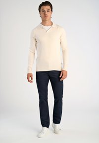 Ljus beige stickad tröja med krage, i kombination med marinblå slim-fit byxor och vita sneakers, med ribbade ärmslut och nederkant.