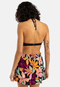 Haut de bikini noir avec un lien au cou et un dos à fermoir, associé à des shorts à motifs floraux multicolores avec des accents roses, oranges et verts.