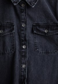 Donkerblauwe denim shirt met een knoopsluiting aan de voorkant, twee borstzakken en zilveren hardware-accenten, voorzien van een klassieke kraag en een gestructureerde stof.