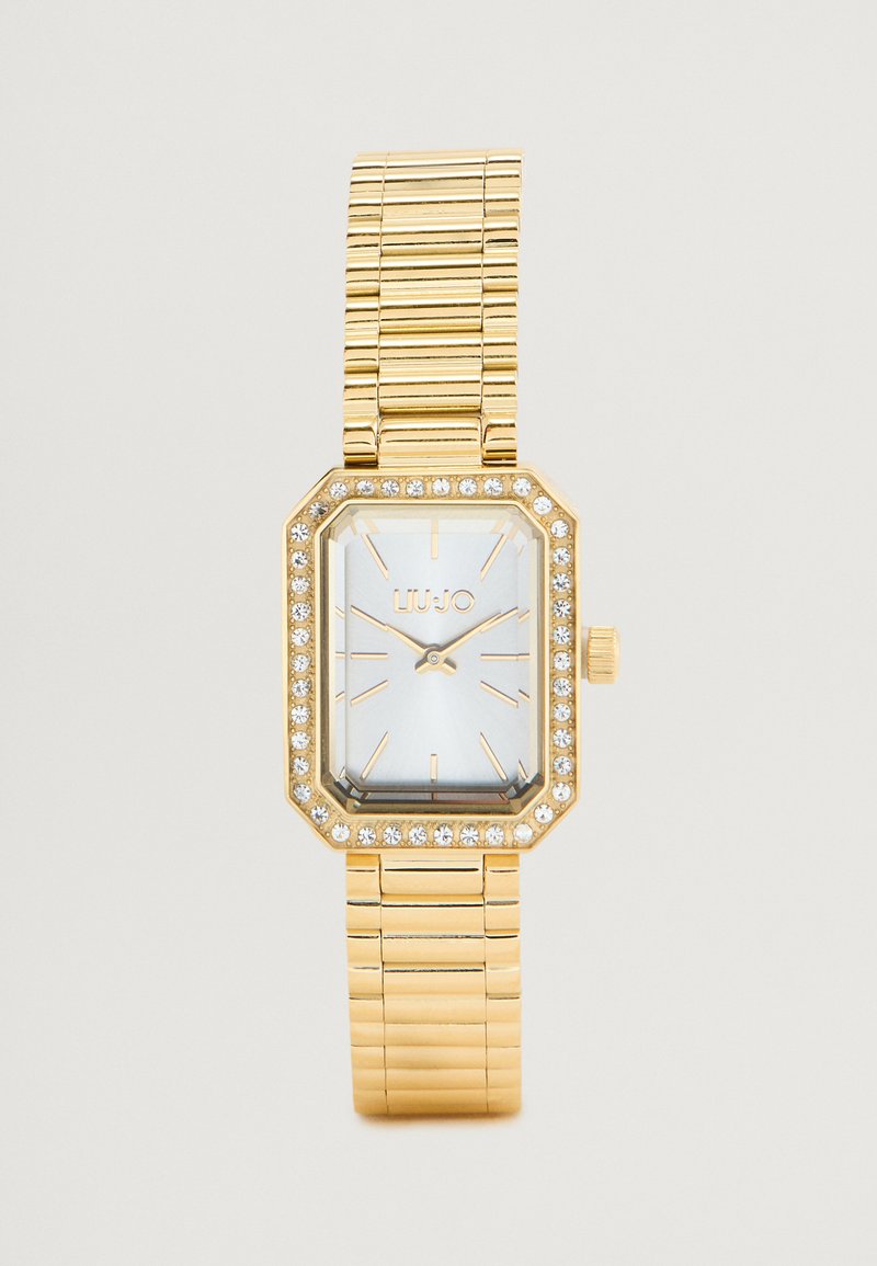 Guldtonet rektangulær ur med en hvid urskive, krystalaccenter omkring bezel og et fleksibelt ledarmbånd. Moderne og strømlinet design.