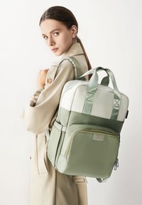 Mochila verde y crema con múltiples compartimentos, correas texturizadas y un sutil acento. Material suave con forma rectangular y doble asa.