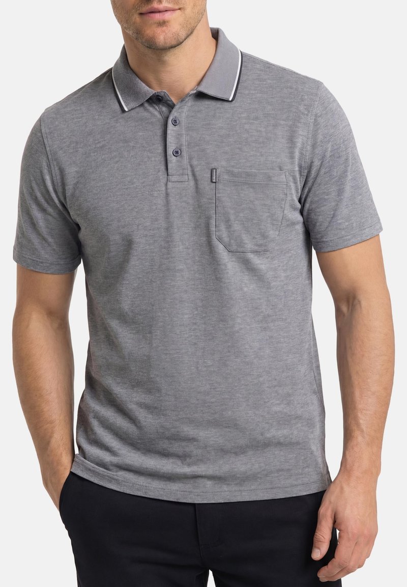 Mężczyzna ubrany w szarą koszulkę polo z krótkim rękawem, kołnierzykiem, trzema guzikami i kieszenią na piersi, w połączeniu z ciemnymi spodniami.