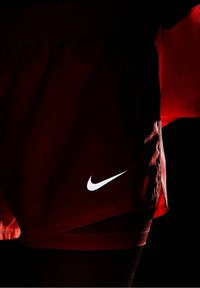Pantalones cortos deportivos rojos con cinturilla elástica y logotipo blanco de Nike en el lado inferior, con una textura suave y un corte sencillo.