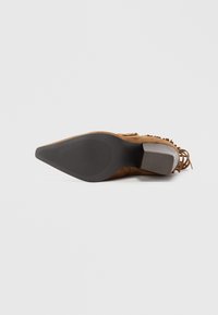 Botine din suede maro cu o talpă texturată, un toc lat și franjuri decorative de-a lungul marginii superioare. Bază plată cu prindere striată.