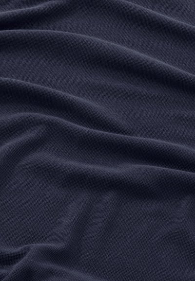 Mørk marineblåt stof med en fin vafletstrikket struktur, der viser bløde folder og blide skygger over overfladen.