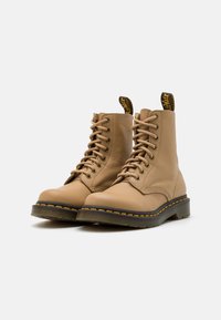 Bottines en cuir tan avec bout rond, lacets sur le devant, couture jaune et languette à motif. Semelle robuste avec un léger talon.