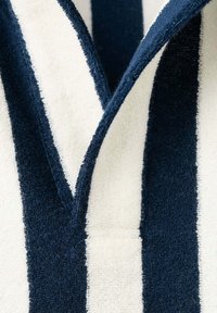 Gros plan d’un tissu avec des rayures verticales en tissu éponge bleu marine et blanc et un détail de chevauchement en forme de V.