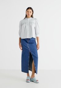 Blouse rayée bleu clair avec des manches bouffantes, associée à une jupe longue en denim foncé avec une fente à l'avant, et des mules à plateforme bleu clair.