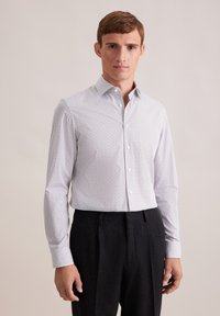 Camicia bianca con un delicato motivo a pois neri, colletto classico, maniche lunghe e vestibilità sagomata, abbinata a pantaloni scuri.