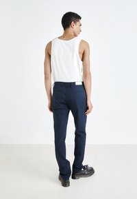 Navy blue pants with a slim fit and side pockets, made from lightweight fabric. Worn with a white tank top and black shoes, viewed from behind.