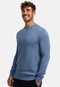 Blå strikket genser med en fiskebensmønster, rund hals, ribbestrikkede mansjetter og hem. Laget av teksturert stoff for ekstra detaljer.