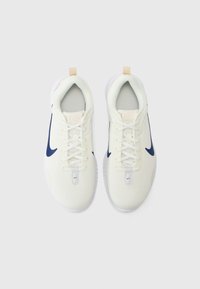 Un par de zapatillas deportivas blancas con logotipos de swoosh en azul marino, cordones blancos y tiradores beige, mostradas desde arriba sobre un fondo blanco.