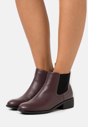 Pair of dark brown leather ankle boots with low stacked heels and black elastic side panels worn on bare legs.