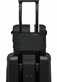 Valigia nera con ruote, dotata di un compartimento superiore morbido, realizzata con materiali riciclati, dettagli neri e superficie testurizzata. Presente un dettaglio a striscia bianca.