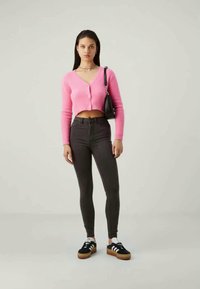 Roza skrajšani cardigan s gumbi, kombiniran z visokim hlačnicami v sivi barvi in črnimi supergami z belimi detajli. Preprosta črna torbica.