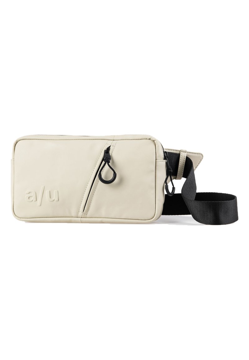 Beige schoudertas met een gladde textuur, voorzien van een diagonale rits, zwarte hardware en een verstelbare schouderriem. Logo is op de voorkant gegraveerd.