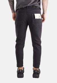 Jeans neri slim fit con vita media, tasche posteriori e etichetta in vita. Il tessuto sembra leggermente texture.