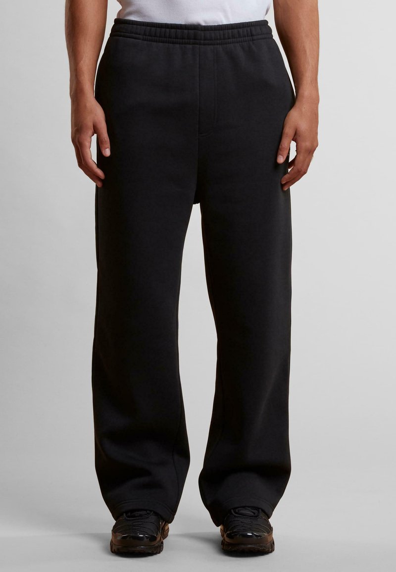 Sorte joggebukser med vid bendesign, elastisk midjebånd og materiale av bomullsblanding. Har en glatt tekstur og ingen synlige logoer.