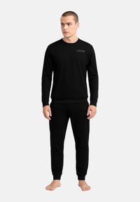 Completo in cotone nero composto da felpa e pantaloni jogger. Girocollo, maniche lunghe, polsini e fascia in vita a coste, marchio minimale sul petto, texture liscia.