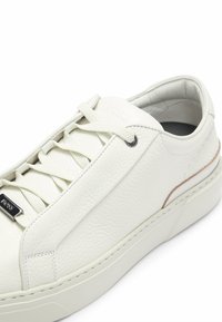 Sneaker bianca in pelle con superficie testurizzata, punta arrotondata, lacci piatti e dettagli in metallo argentato. Presenta una suola in gomma sottile.