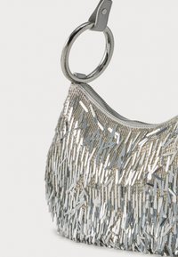 Geantă argintie cu paiete, textură cu franjuri, formă rotundă, închidere cu fermoar și mâner circular din metal.