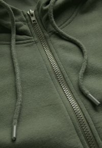 Olivgrön hoodie med fullängdsdragkedja, försedd med en texturerad yta och dragskor, som visar upp en slät och enkel design.
